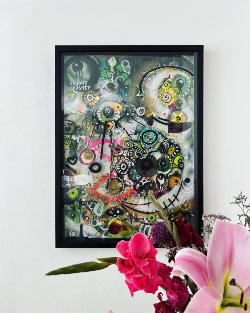 Kim's artwork titled 'Vanity' which is filled with figurative, abstract, and complex forms resembling eyes, sits on a white wall with a vase of flowers showing in the foreground