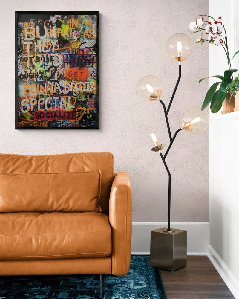 A mock-up of Kim's mixed media piece titled 'Delinquency in a room with a brown sofa and an abstract modern floor lamp with big bulbs.