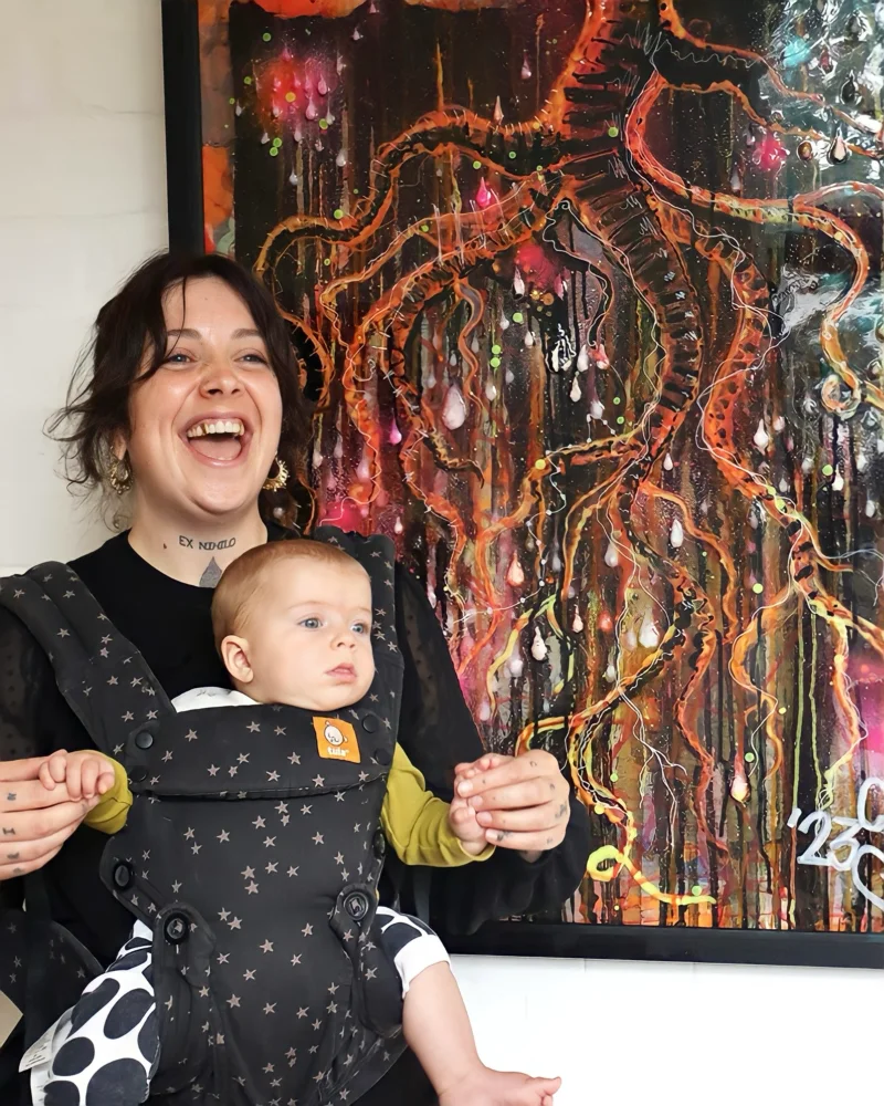 Kim stood in front of her artwork 'Antagony' with a baby in a sling on her front. The artwork is on display at Hereford College of Arts for her exhibition 'Everything I ever made, almost'