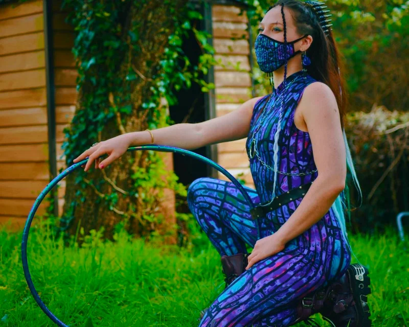 An alternative model posing with a hula hoop, wearing a catsuit and mask featuring Kim's designs. She wears New-Rock boots and a hairclip laden with bullets.