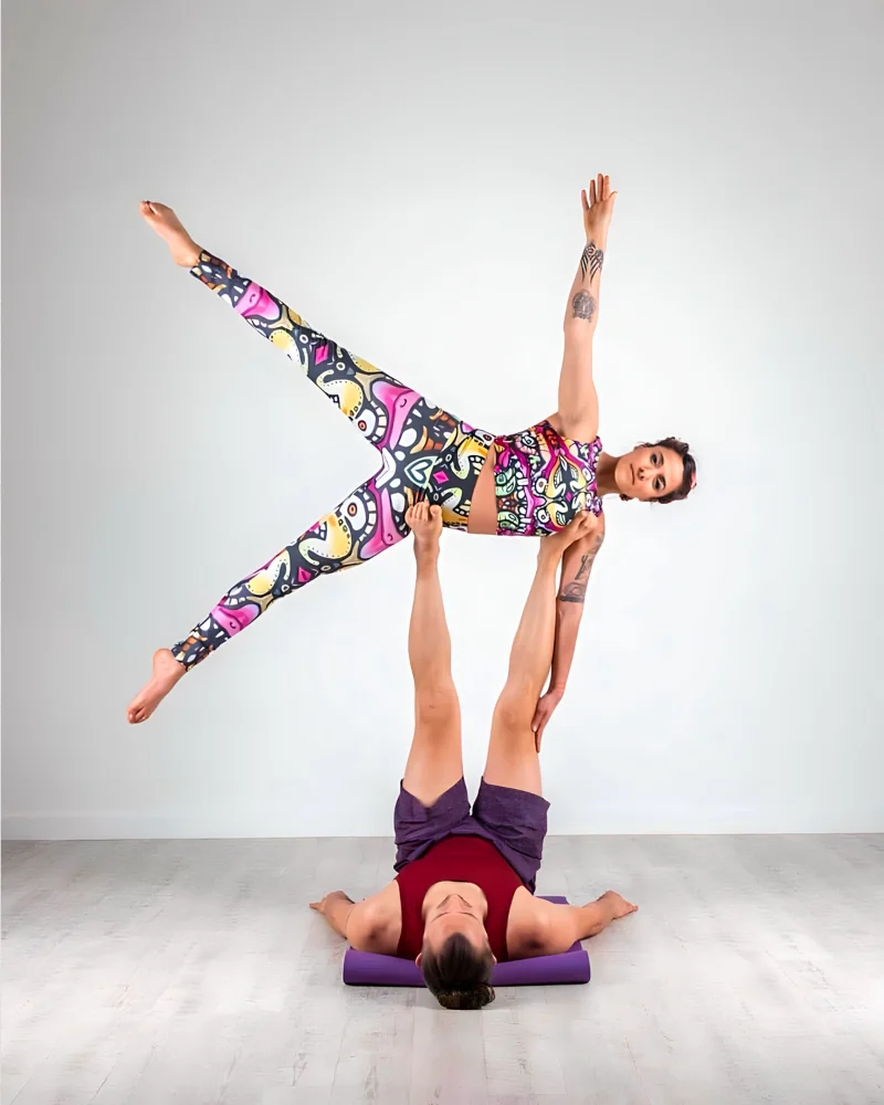 A gymnast wearing lycra leggings and a crop top designed by Kim. She balances in a star shape on top of a mans legs.